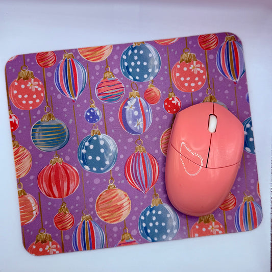 Pink computer mouse on a purple mouse pad with colorful Christmas ball design