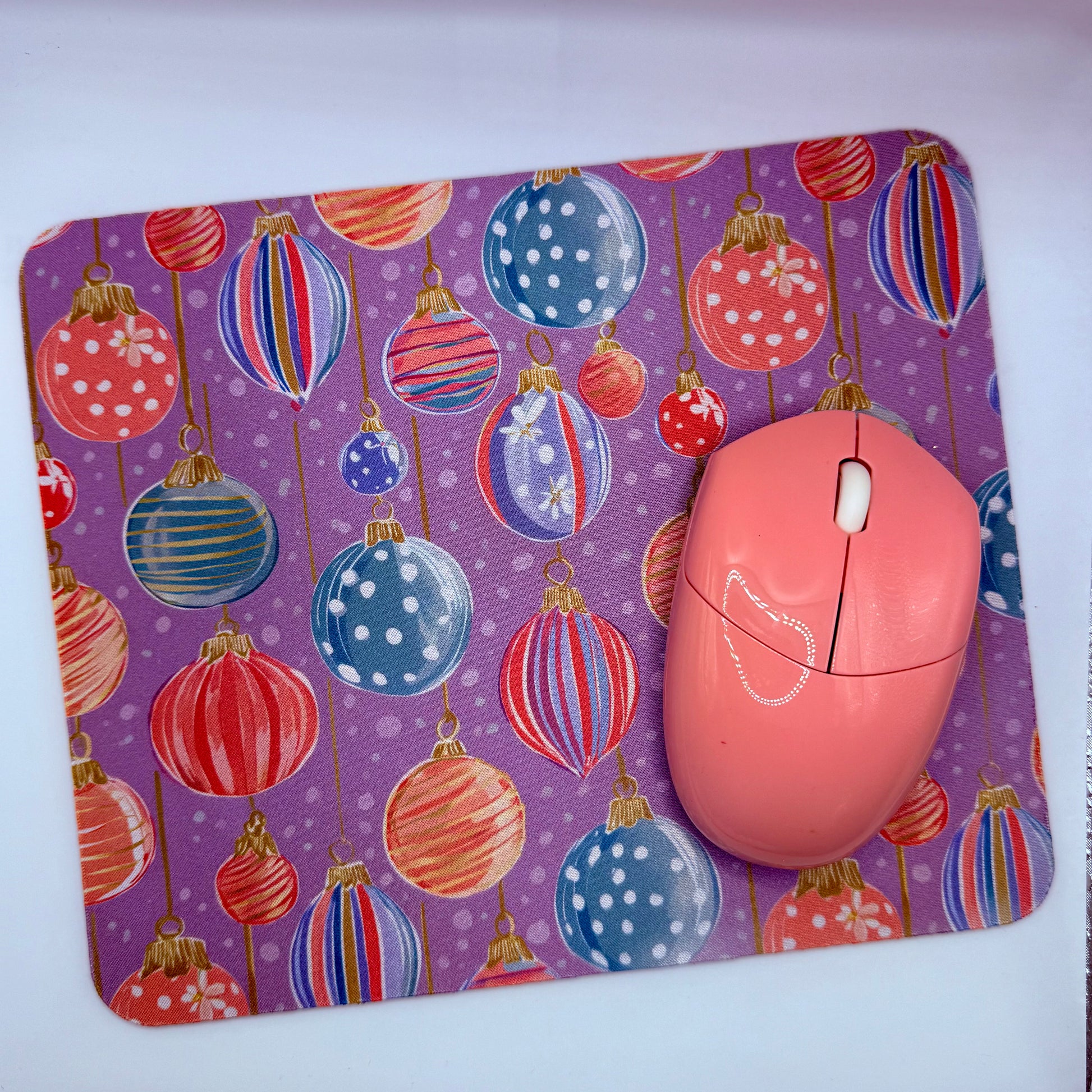 Pink computer mouse on a purple mouse pad with colorful Christmas ball design
